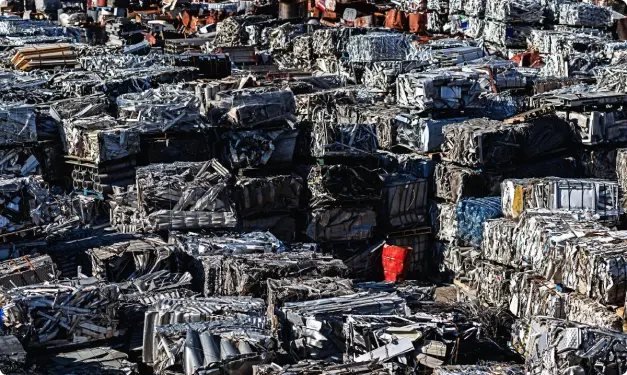 Large metal scrap yard with stacked, pressed metal blocks in various colors and structures.